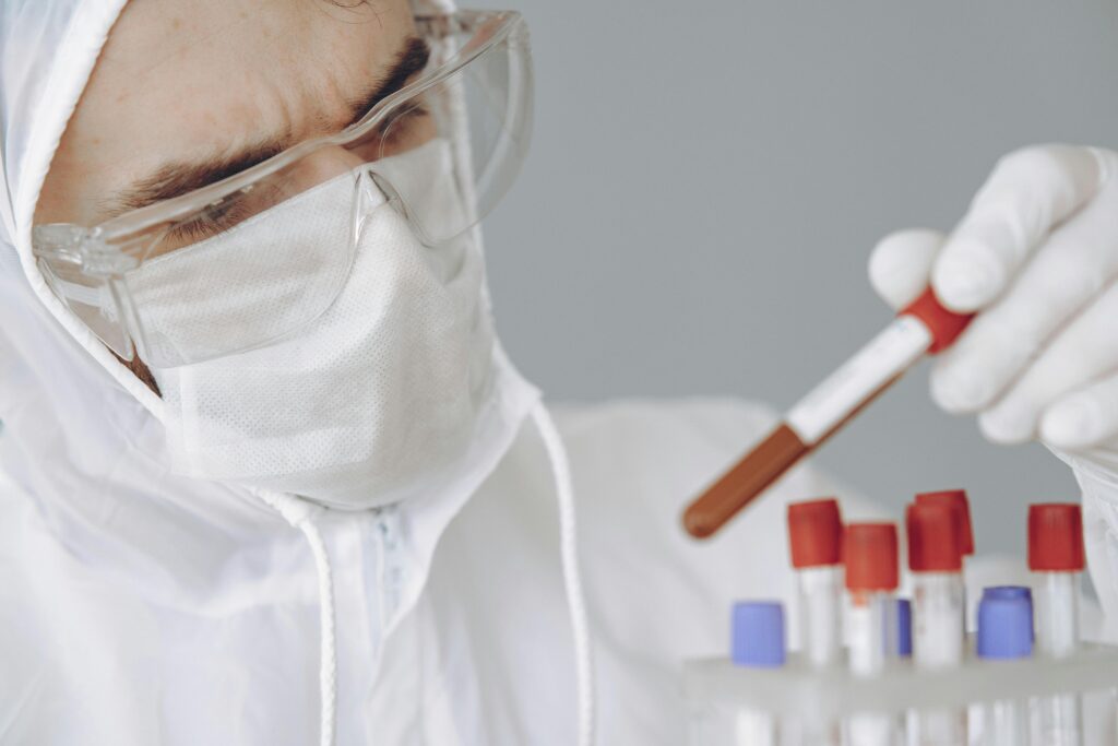 Scientist in PPE examining test samples in a laboratory setting.